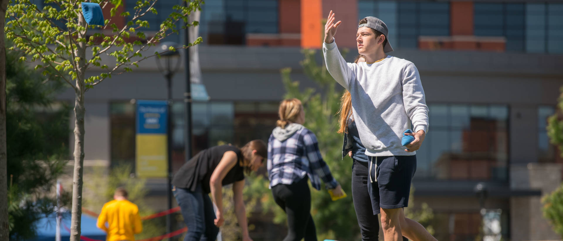 Male student tossing bags for bean bag game on campus mall, spring