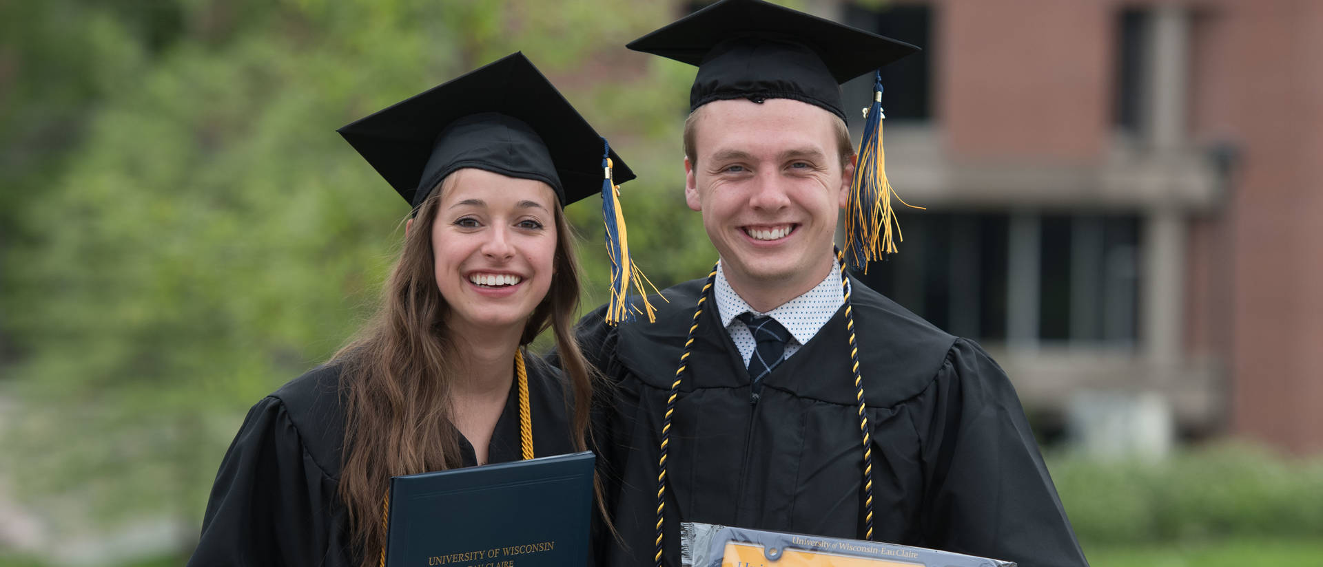 Pair of gradautes holding up the Blugold lisence plate. 