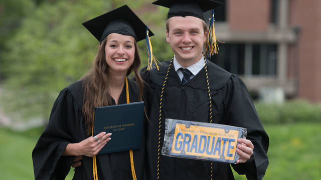 Pair of gradautes holding up the Blugold lisence plate. 