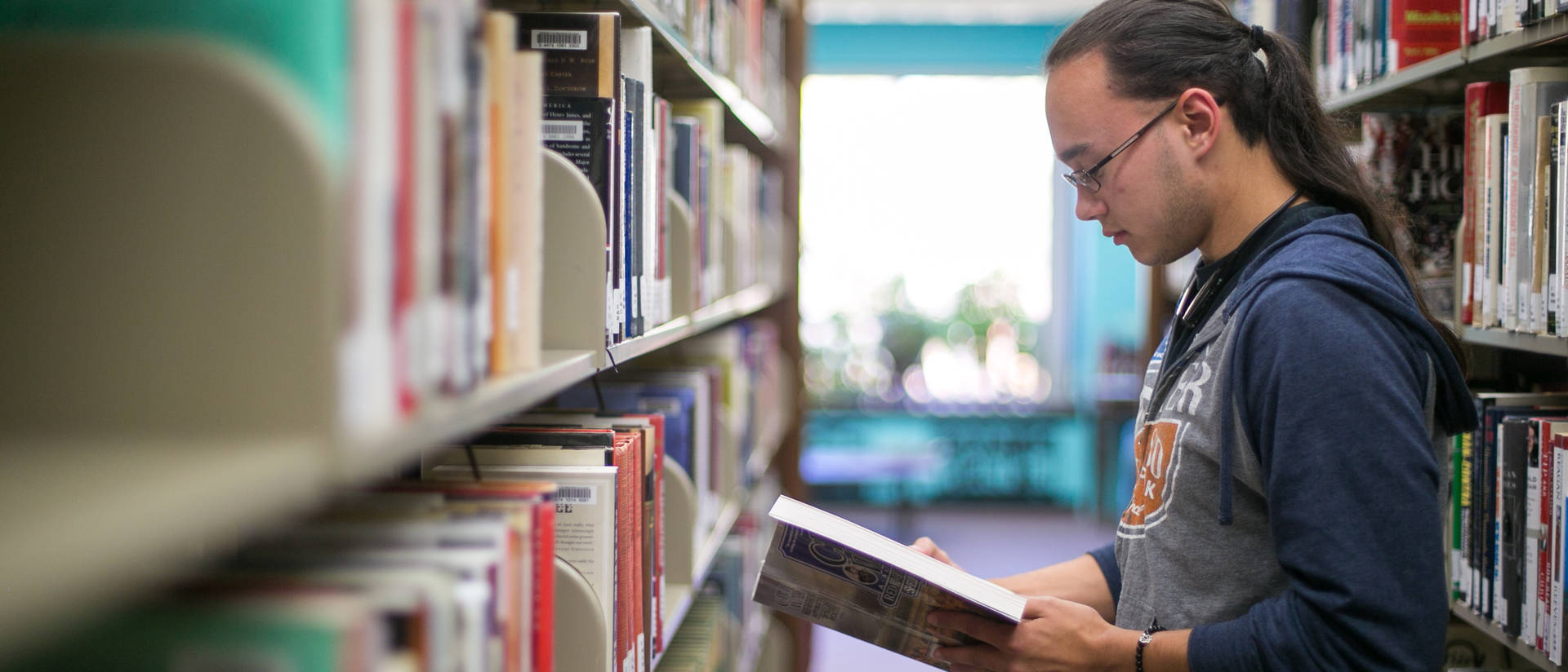 Male student in the library stacks looking at a book