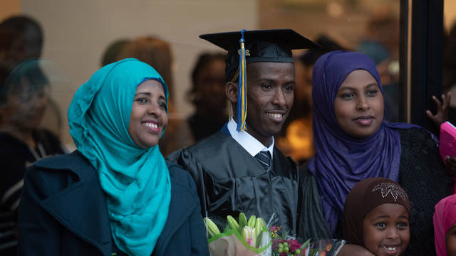 Student wearing graduation cap and gown and posing for photo with family