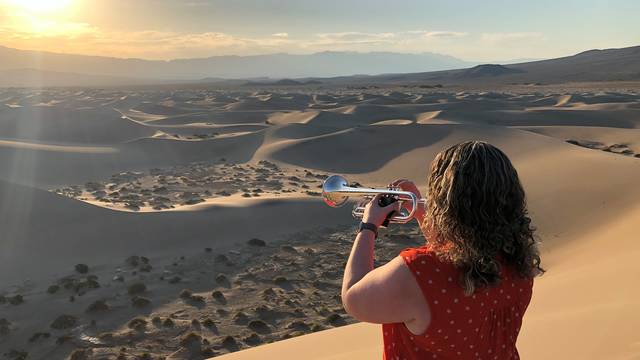 Woman plays trumpet in desert.