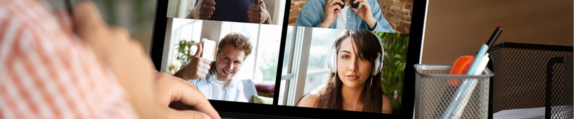 Student sitting at a table participating in an online meeting with 4 individuals displayed on his computer