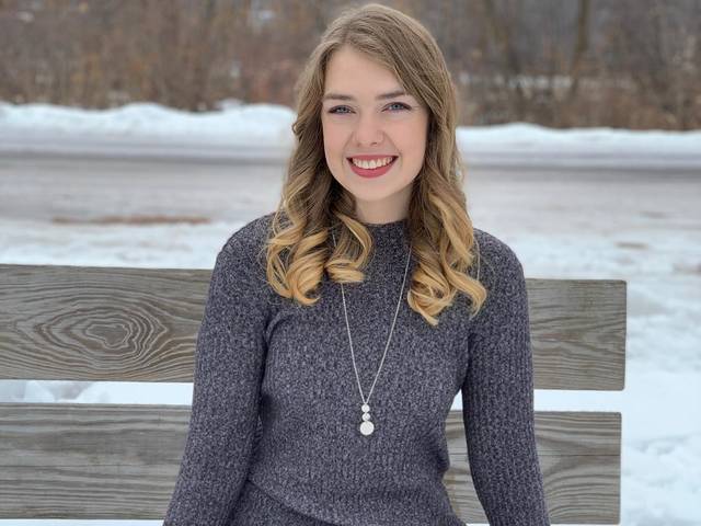 Dana smiling for a portrait on a bench in the winter