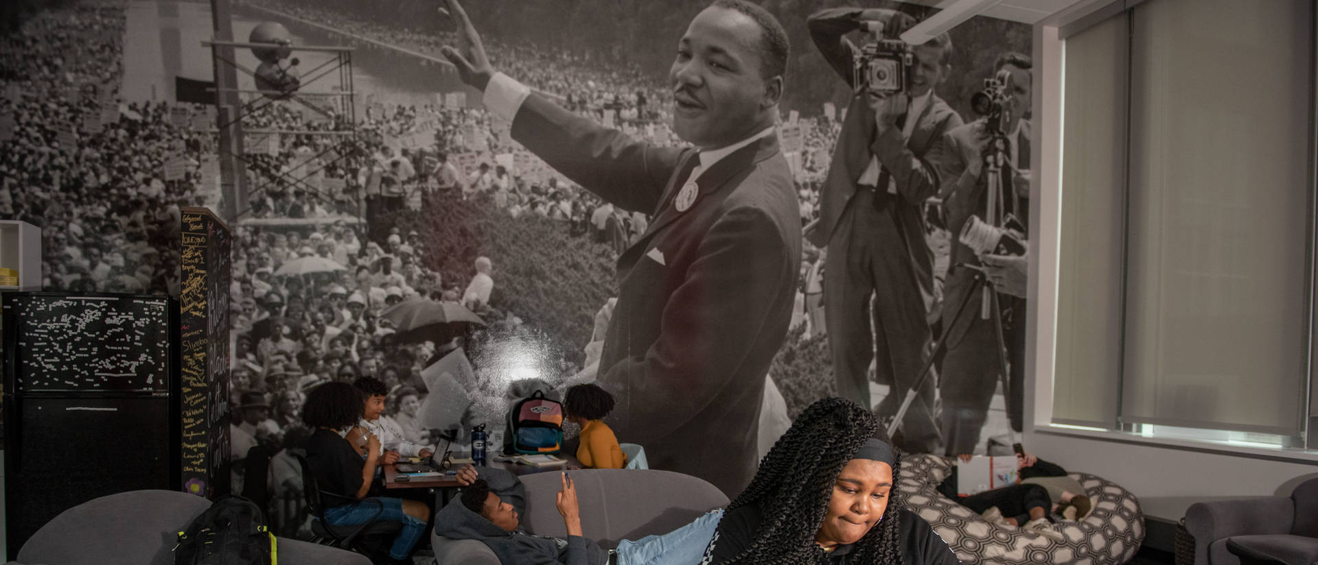 Student sitting at laptop in UWEC Black Cultural Center, MLK mural on the wall