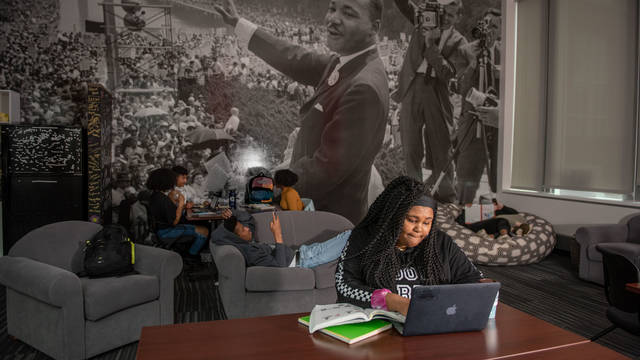 Student sitting at laptop in UWEC Black Cultural Center, MLK mural on the wall