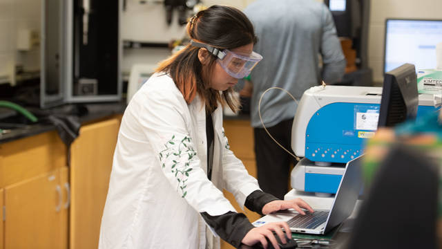 Woman in goggles working at laptop in lab.