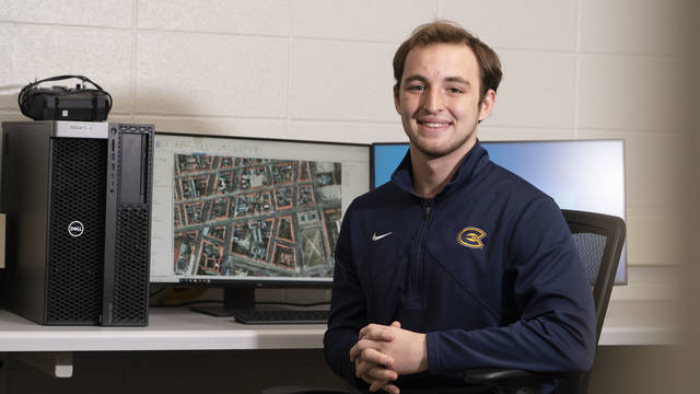 Male student smiling in a computer lab, sitting at a work station