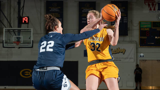 Women's basketball player holds ball and faces defense during a game.