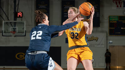 Women's basketball player holds ball and faces defense during a game.