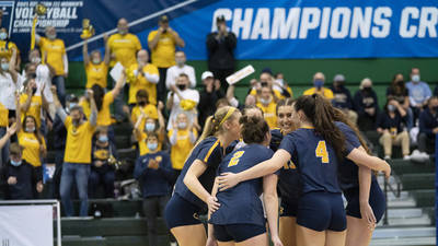 Volleyball players huddle at the national championship game with fans cheering in the background.