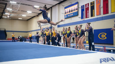 Gymnast does floor routine with teammates cheering her on.