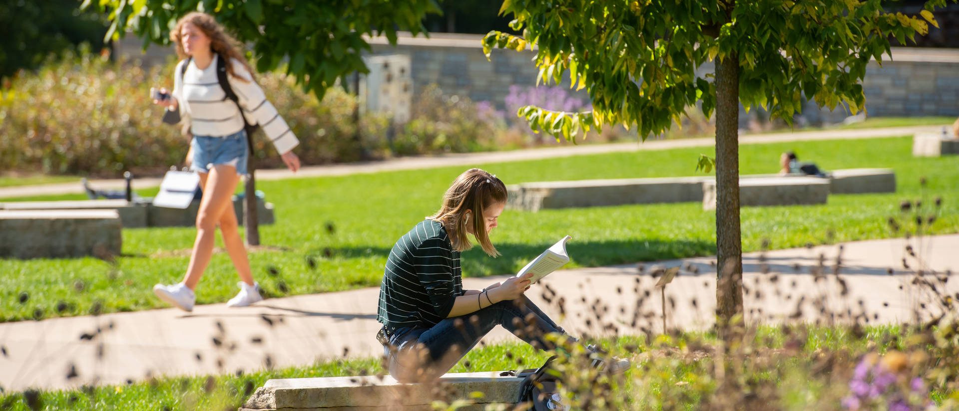 Student reads a book while sitting outside on a sunny day.