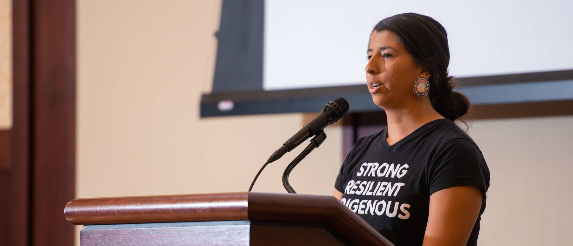 Woman speaks at a podium on Indigenous People's Day