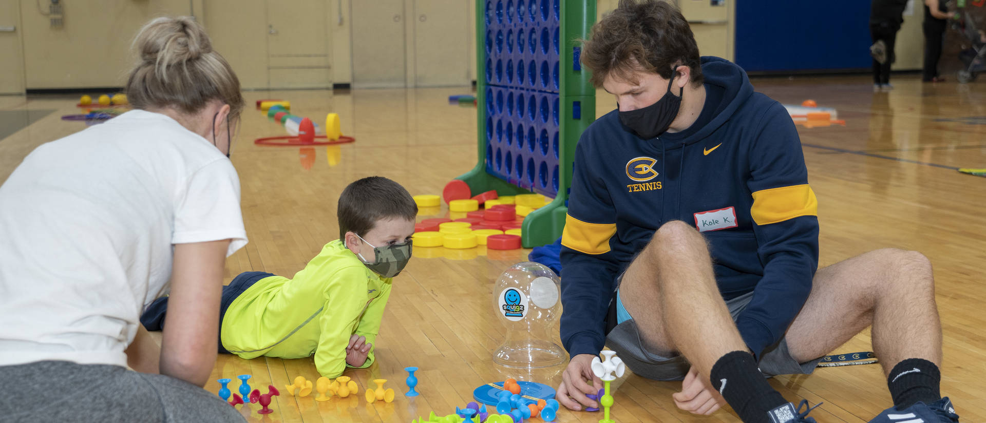 Kinesiology students sit on the floor working with a participant on physical activity stations in the McPhee Physical Education building.