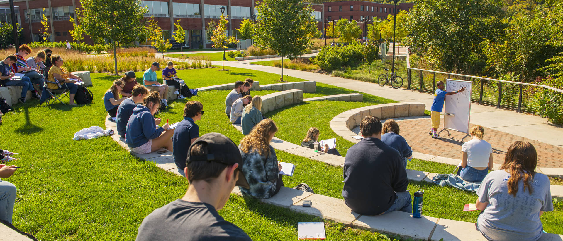 A class sits in the outdoor classroom on campus during a sunny day.