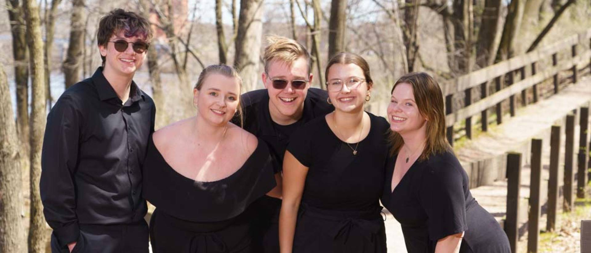 A small group of chamber ensemble members wearing all black pose for a photo outside