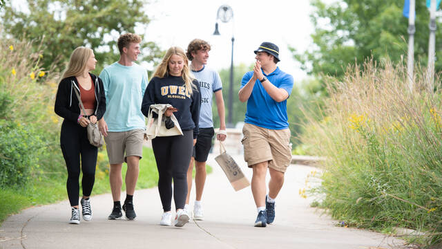 male and female students walking on campus sidewalk by tall grass