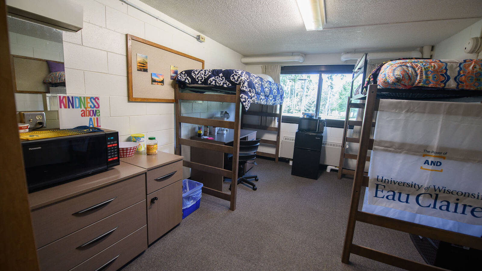A double dorm room showing two lofted beds, a desk, a dresser and mini fridge