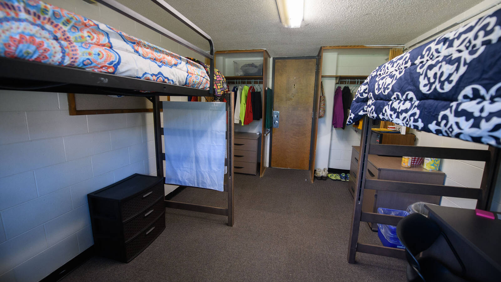 A view of a dorm living space facing the entrance, where both closets and dressers can be seen in a lofted arrangement