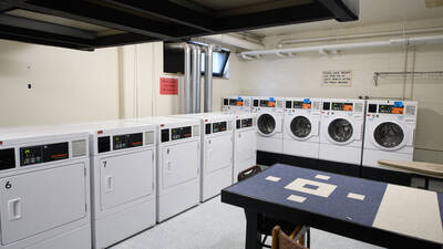 Laundry room featuring multiple commercial washing machines and dryers, plus a table and chairs