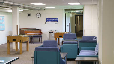 A common space in Sutherland Hall with groups of upholstered seating, two foosball tables, and a piano