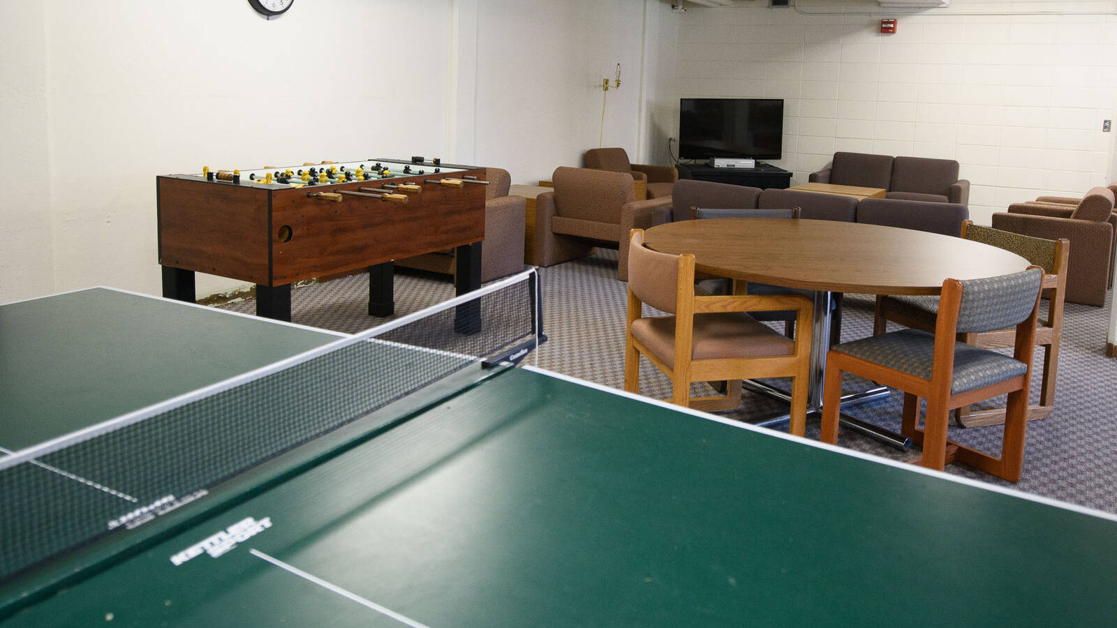 A common space in a residence hall with ping pong, foosball, a TV and seating