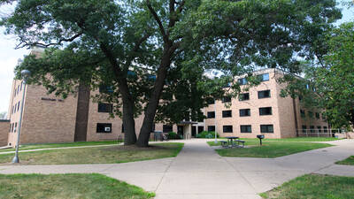 Exterior view of Bridgman Hall, a brick building with lots of windows and a big tree and picnic table in front.
