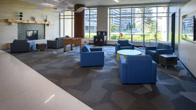 Lobby area of The Suites residence hall, with large windows, a fireplace and lounge seating