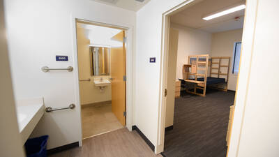 Hallway showing an open door into a bedroom next to an open door to the bathroom with a sink and mirror