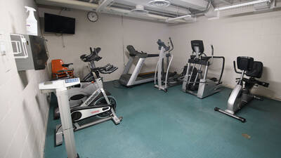 A room with exercise equipment including a treadmill, stationary bikes, and ellipticals.