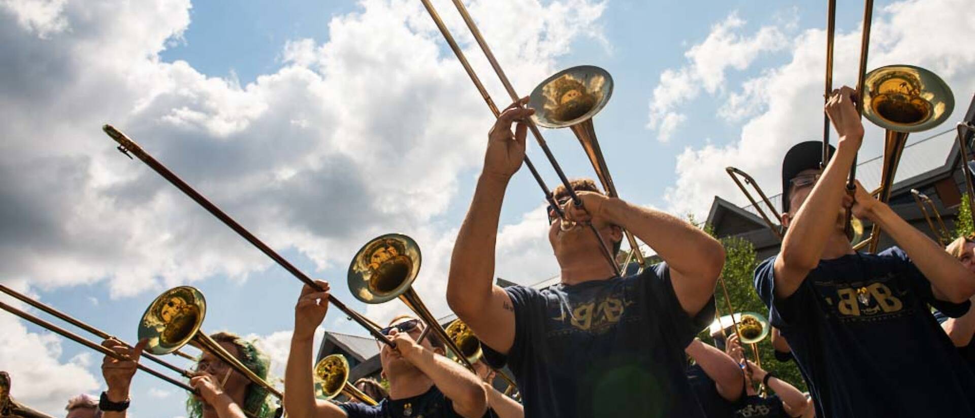 Horns playing in a marching band with sky in the background.