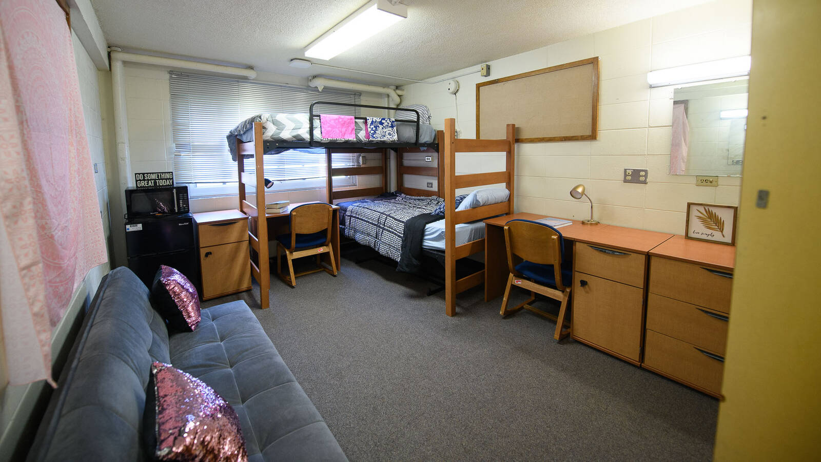 A room in Governors Hall with two bunked beds, two desks, a mini fridge and a couch.
