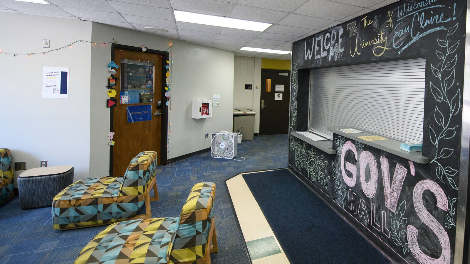 Lobby area of Governors Hall with colorful chairs and a welcome desk surrounded by a chalkboard wall decorated with a "Welcome to UWEC" message.