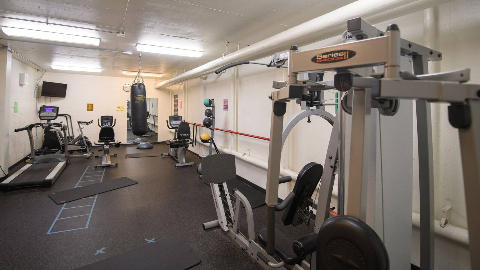 Fitness room in Governors Hall with treadmill, stationary bikes, stair stepper, punching bag, exercise mats, cable machines, and medicine balls.