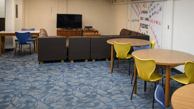 Common space in Governors Hall with chairs, tables, and a TV.