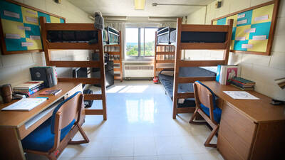 Horan Hall Room with two beds lofted bed, chairs, desks, and a big window. A futon is under one bed and a TV and mini fridge is under the other.