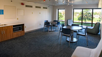 Lounge space in Towers Hall with tables and chairs, big windows, and a microwave and sink.