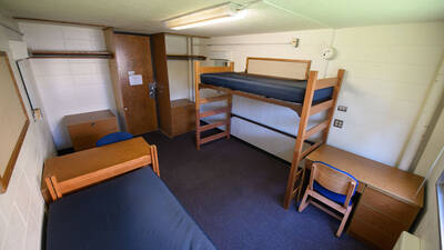 Murry Hall room (viewed from the wall opposite the door) with two beds, chairs, desks, dressers, and closet hanging space.