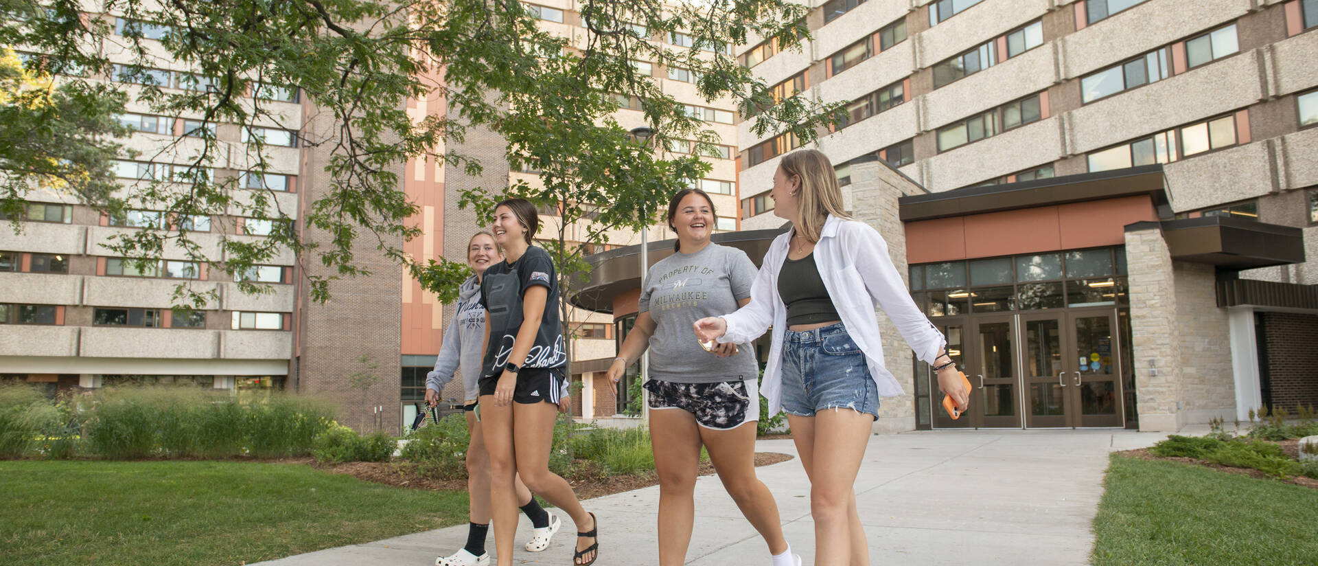 Students walk together out of a residence hall on a sidewalk.