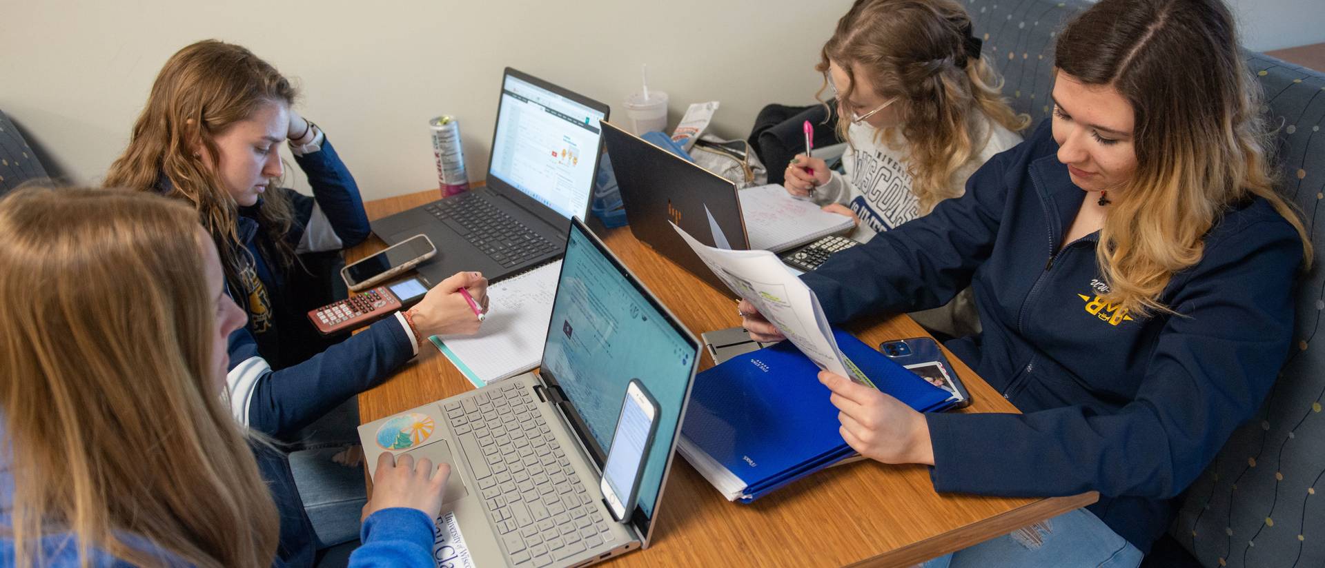 A group of four students share a booth and study on their laptops