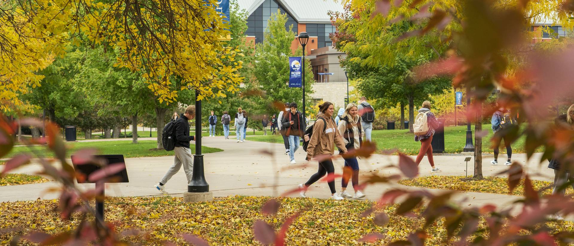 Students walking to class on a fall day, with trees changing to orange and leaves on the ground