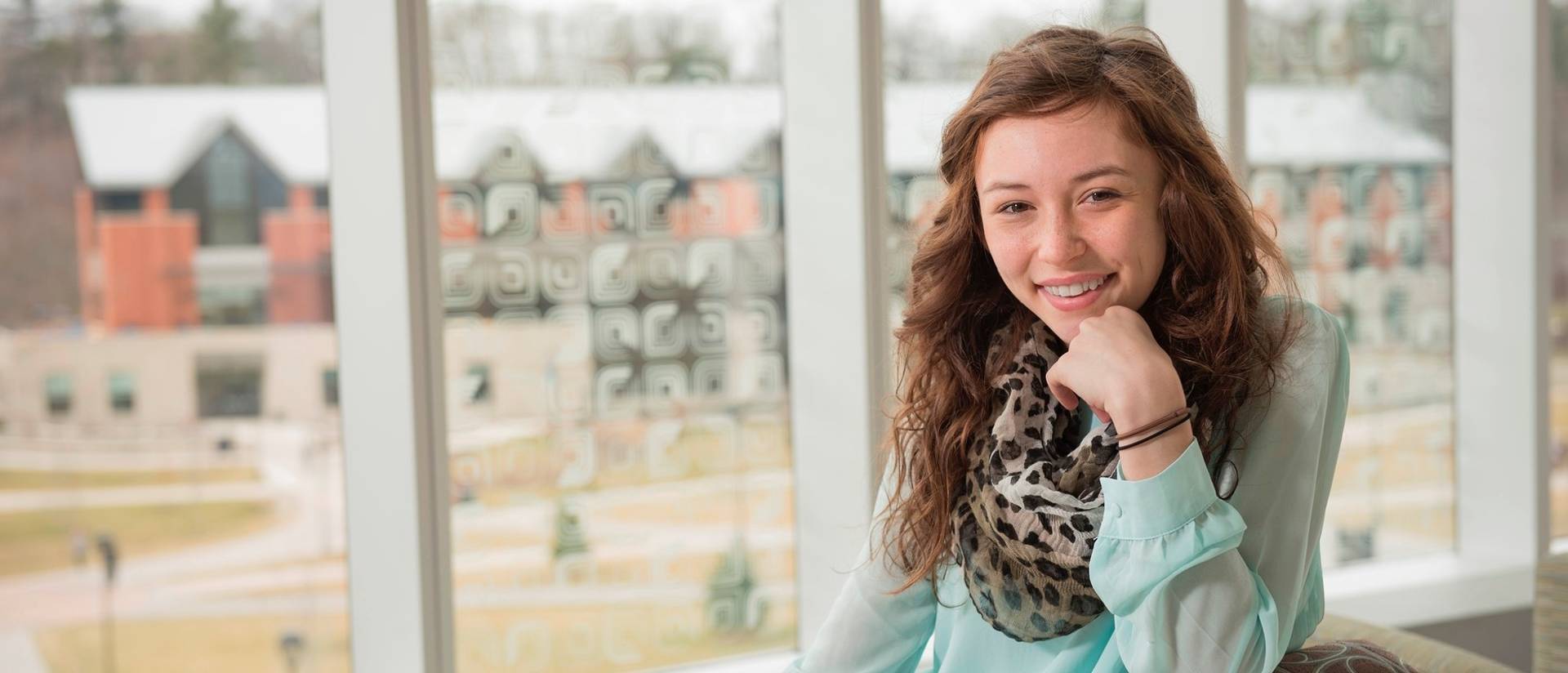 A portrait of graduate Maddy Mahoney in Centennial, smiling into the camera with her chin on her hand.