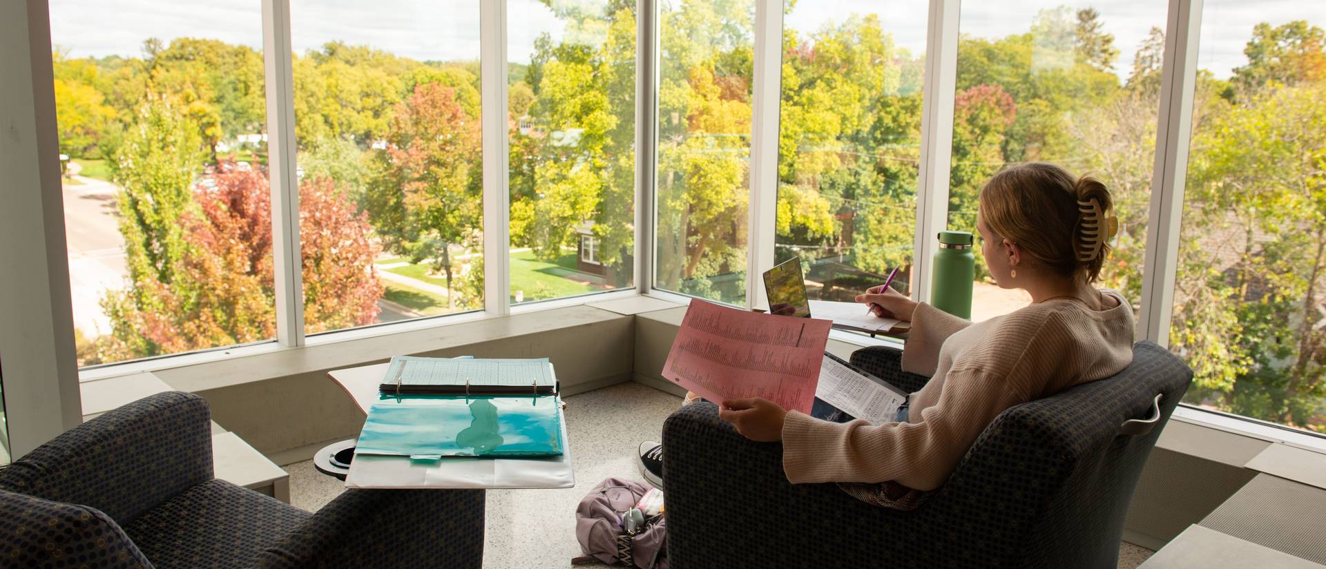 A student studies in front of a lot of windows in a building on campus