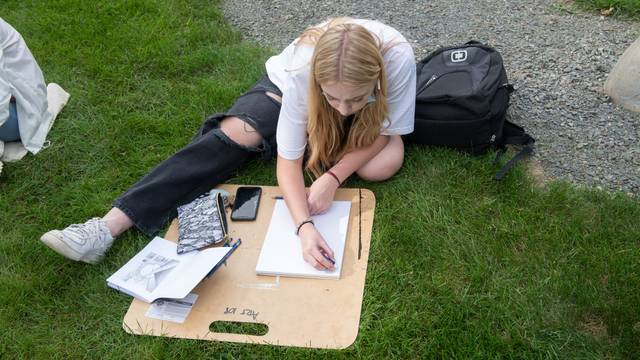 Student draws using a clipboard in the grass for an outdoor art class