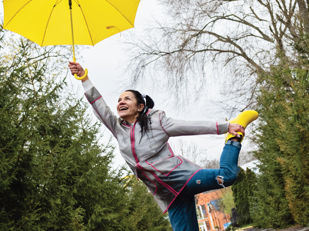 A young woman hold an umbrella in the air with a happy expression on her face.