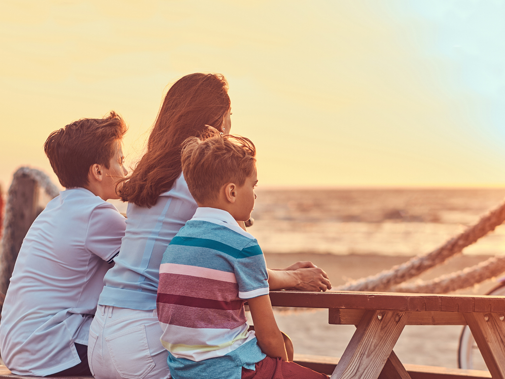A mother and her two sons sit at a picnic table at the beach and watch the sunset.