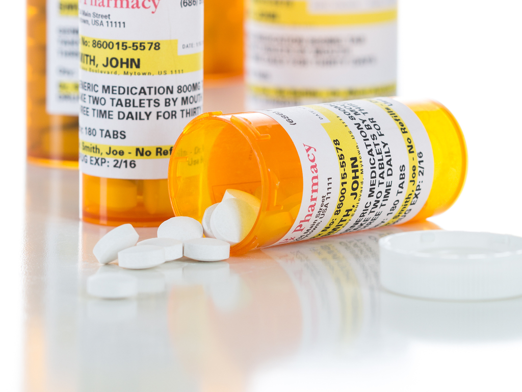 A bottle of pills lays open on a table surrounded by three other bottles of pills.