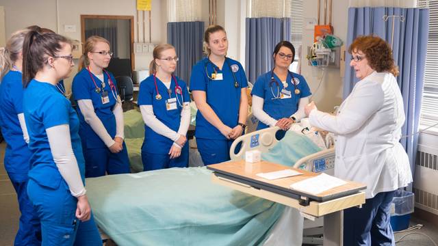 Nursing students standing around a hospital bed looking at the instructor demonstrating with a patient.