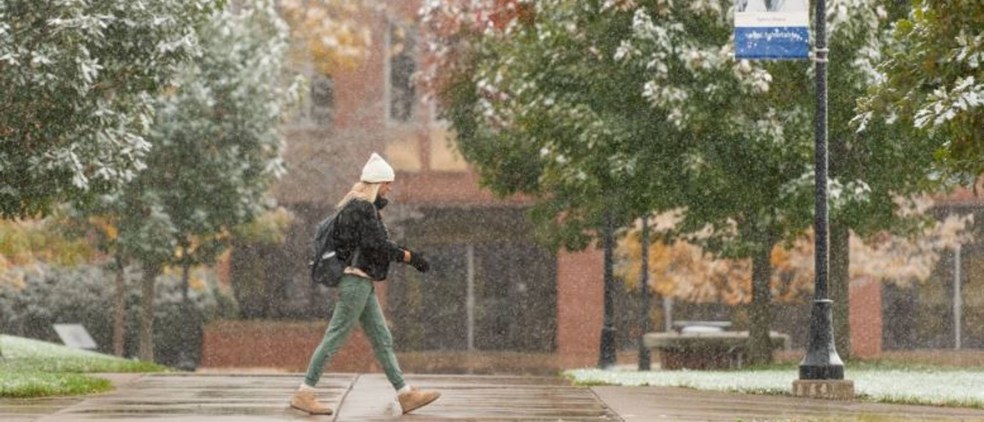 College students walking past building while snow is falling.
